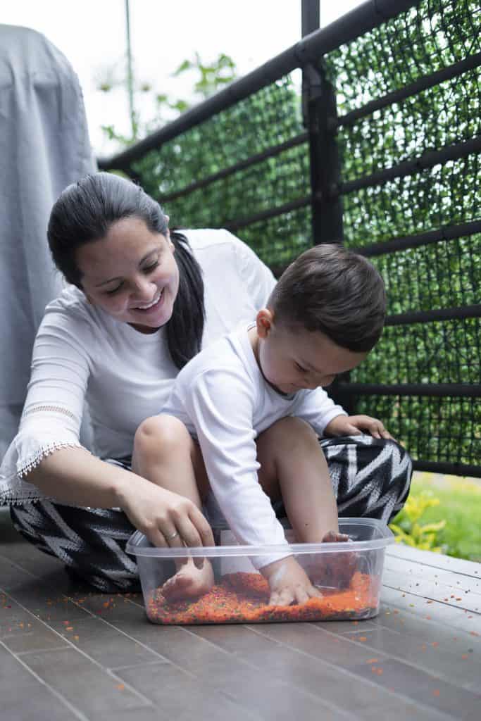 Young Latin mother with her son, both from Bogota Colombia, play on the balcony of the house with their colored therapeutic rice to improve their motor skills and enjoy the activity