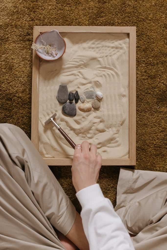 A calming zen garden setup with sand and rocks, featuring a hand arranging with a rake.
