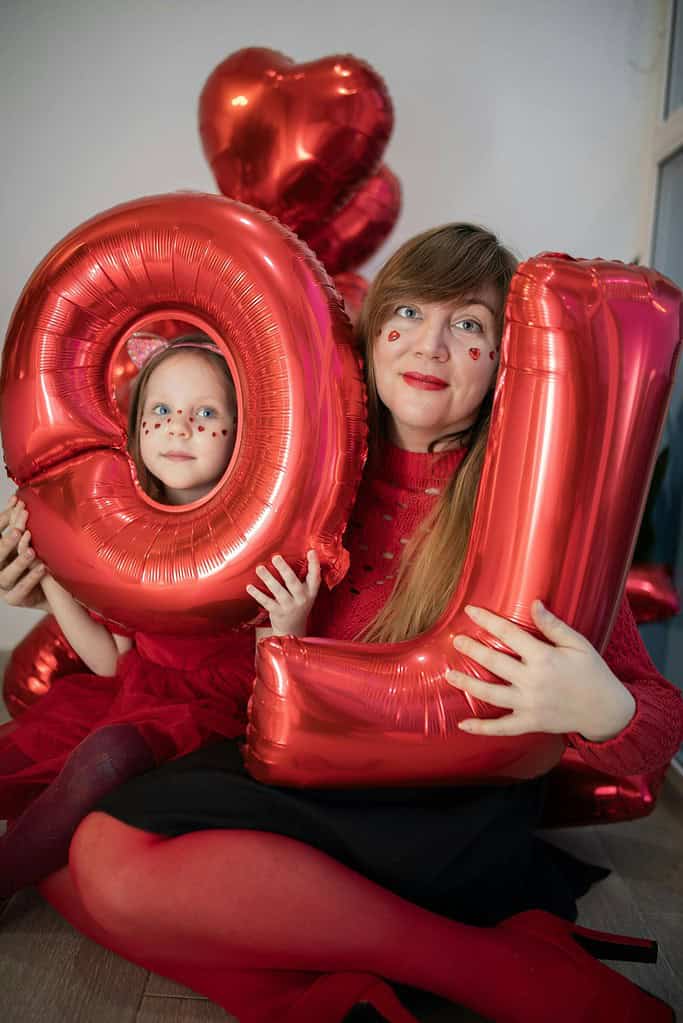 A cheerful mother and daughter posing with red balloon letters indoors. Perfect for festive stock photos.